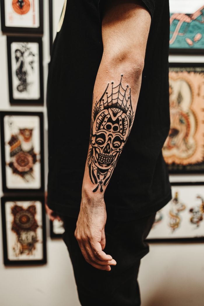 services-img Detailed close-up of a man's arm with an intricate skull tattoo in an artistic setting.