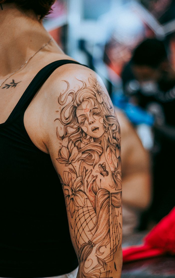 services-02 Close-up view of a detailed floral and portrait tattoo on a person's upper arm.